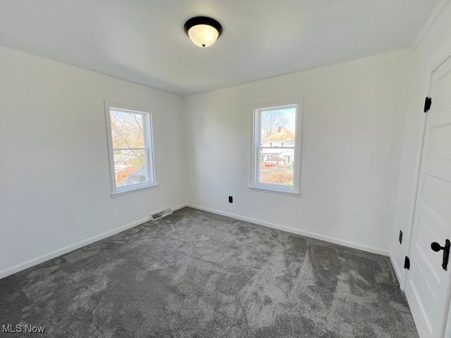 carpeted empty room featuring plenty of natural light, baseboards, and visible vents