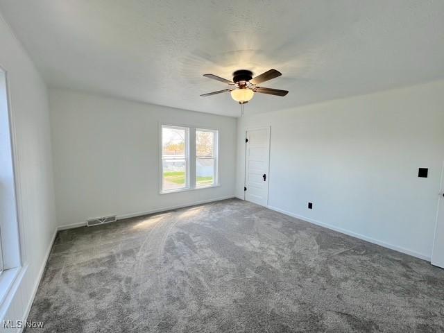 carpeted spare room featuring baseboards, a ceiling fan, and visible vents