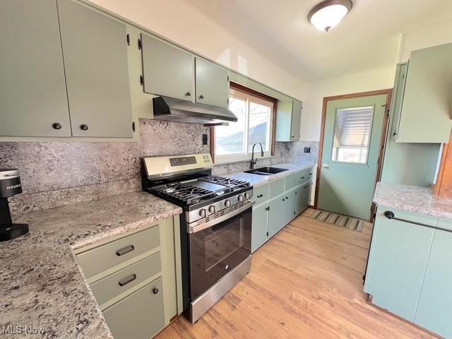 kitchen with under cabinet range hood, a sink, light wood-style floors, gas stove, and tasteful backsplash