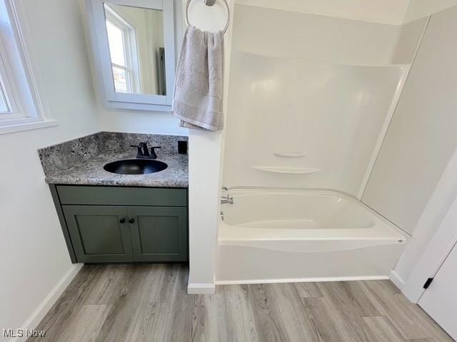 bathroom featuring baseboards, bathing tub / shower combination, wood finished floors, and vanity