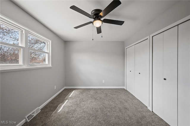 unfurnished bedroom with baseboards, multiple closets, visible vents, and carpet flooring