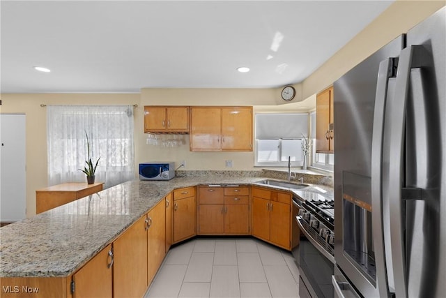 kitchen with a sink, stainless steel appliances, light tile patterned flooring, light stone counters, and a peninsula