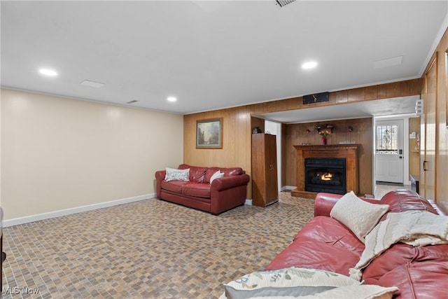 living room with recessed lighting, wood walls, crown molding, baseboards, and a lit fireplace