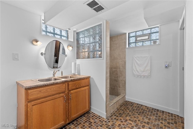 full bath with baseboards, visible vents, a tile shower, and vanity