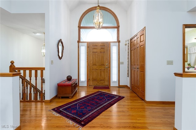 foyer with baseboards, wood finished floors, high vaulted ceiling, and a chandelier