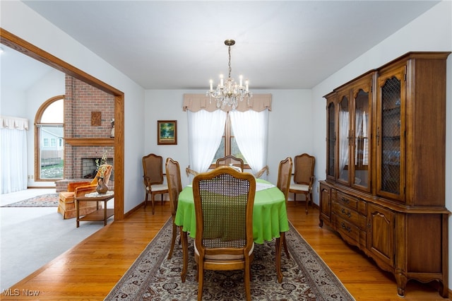 dining area featuring baseboards, a notable chandelier, light wood finished floors, and a fireplace