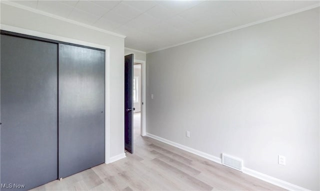 unfurnished bedroom with light wood-style flooring, baseboards, visible vents, a closet, and ornamental molding
