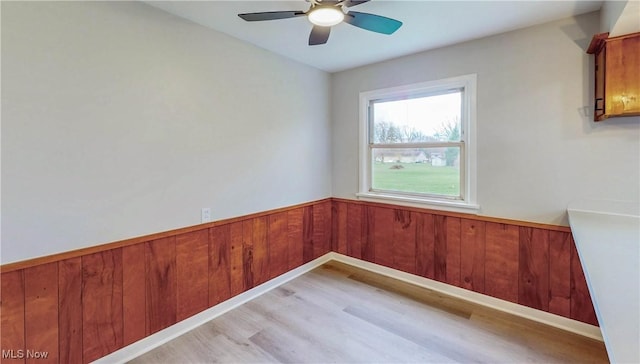 spare room featuring light wood-type flooring, a ceiling fan, wooden walls, and a wainscoted wall