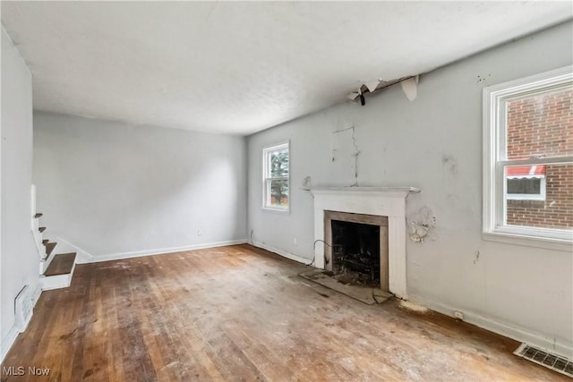 unfurnished living room with baseboards, wood finished floors, visible vents, and a fireplace