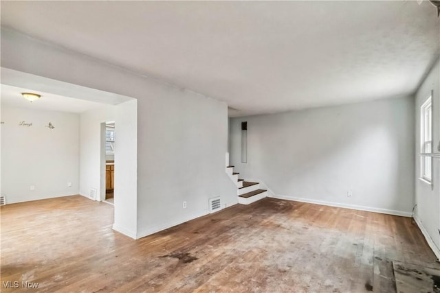 spare room featuring wood finished floors, visible vents, stairs, and a healthy amount of sunlight