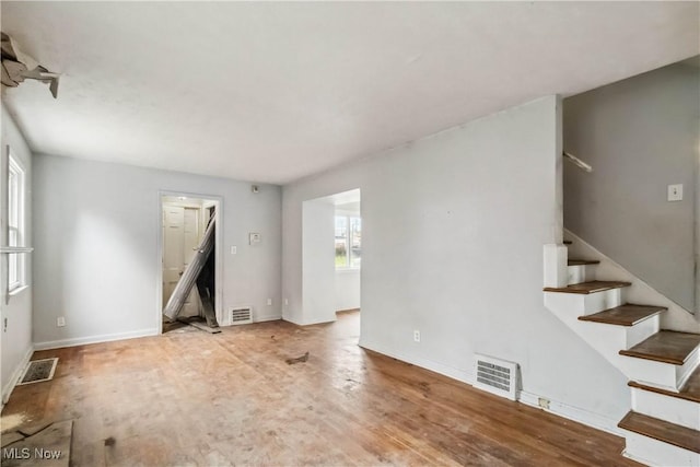 unfurnished living room featuring stairway, visible vents, and plenty of natural light