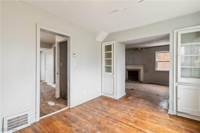 unfurnished room featuring light wood-style flooring, visible vents, and a fireplace