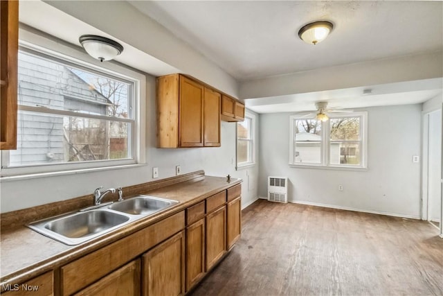 kitchen featuring brown cabinetry, wood finished floors, a sink, and heating unit