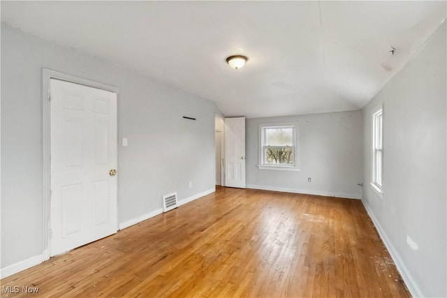 spare room with baseboards, vaulted ceiling, visible vents, and light wood-style floors