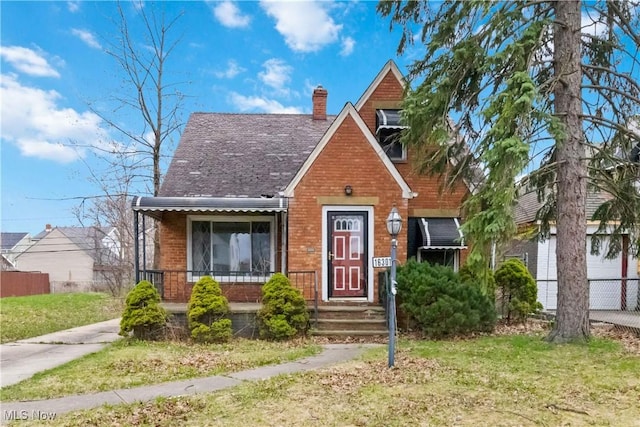 view of front facade featuring brick siding, a chimney, a front yard, and fence