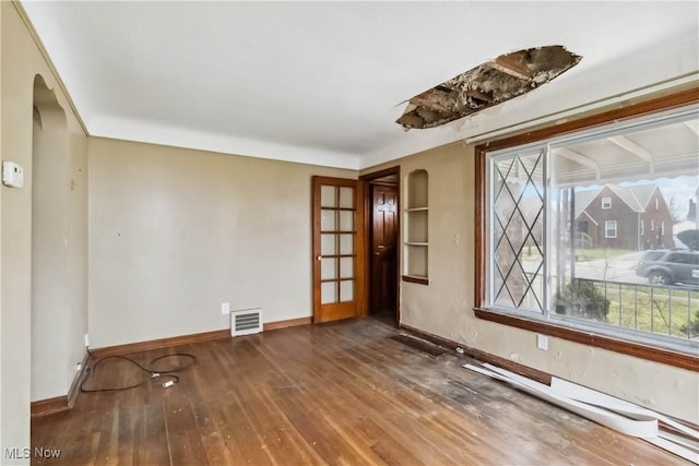spare room featuring arched walkways, wood-type flooring, baseboards, and visible vents