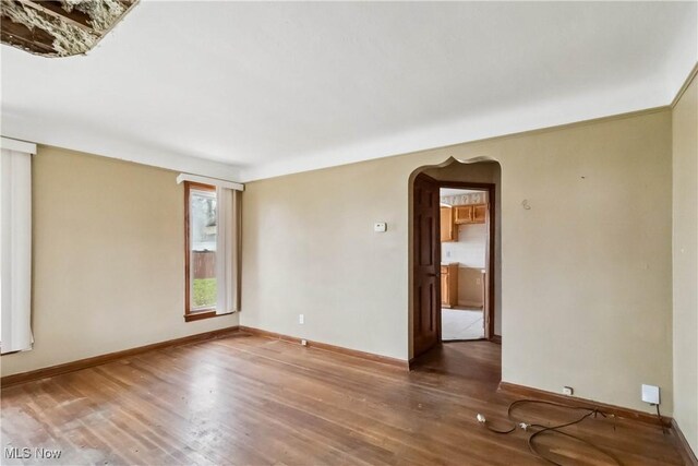 empty room featuring baseboards, wood finished floors, and arched walkways