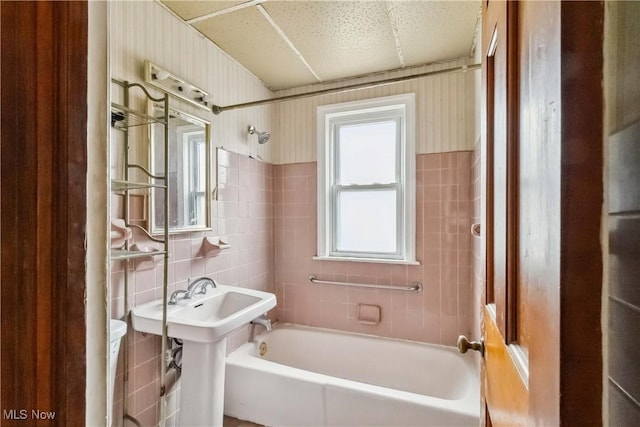 bathroom with tile walls, wallpapered walls, shower / bath combination, and toilet