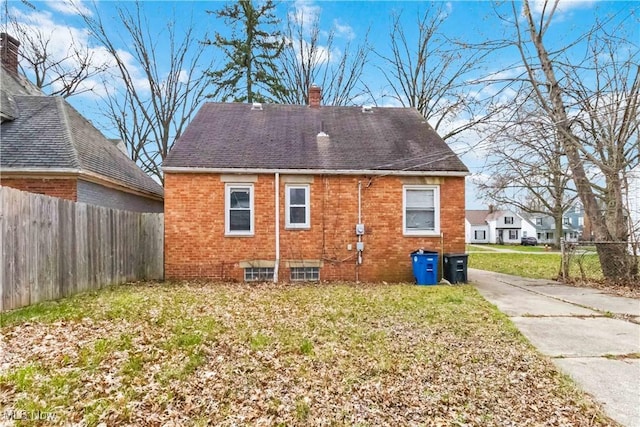 rear view of house with brick siding, a yard, a chimney, and fence