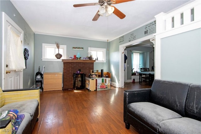 living area featuring wood-type flooring, a brick fireplace, ornamental molding, and ceiling fan