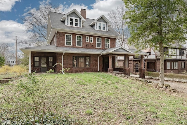 view of front of home featuring a chimney, a front lawn, a shingled roof, covered porch, and brick siding
