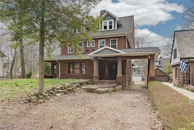 view of front of house featuring a chimney, driveway, covered porch, an outdoor structure, and brick siding