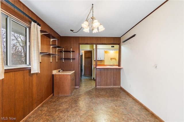 kitchen featuring an inviting chandelier, open shelves, wooden walls, baseboards, and brown cabinetry