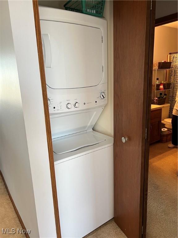 washroom featuring stacked washer and dryer, laundry area, and light colored carpet