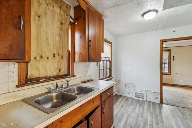 kitchen featuring backsplash, light countertops, visible vents, a sink, and light wood-style flooring