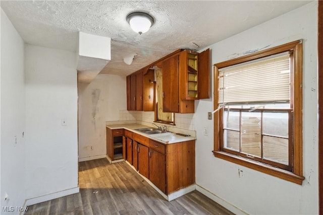 kitchen with a sink, a textured ceiling, wood finished floors, brown cabinetry, and light countertops