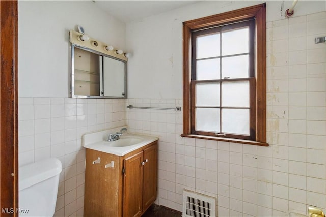 half bath featuring toilet, tile walls, wainscoting, visible vents, and vanity