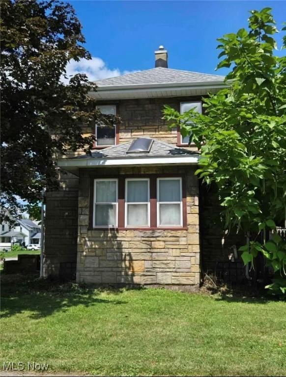 405 Oak Knoll Ave SE, Warren, OH 44483 - view of home's exterior with stone siding, a lawn, a shingled roof, and a chimney