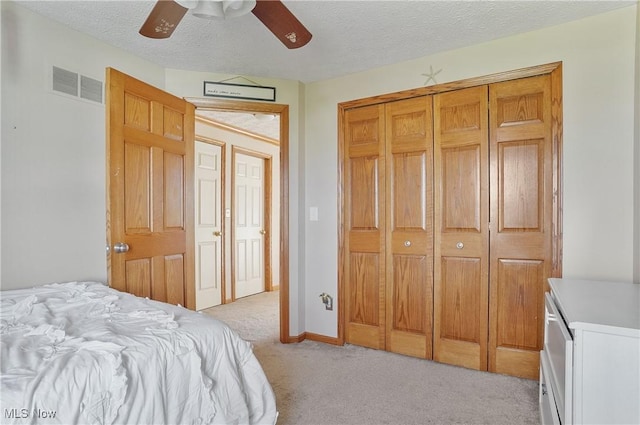 bedroom featuring light colored carpet, a textured ceiling, visible vents, and a closet