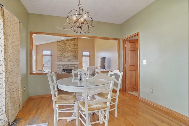 dining space with baseboards, visible vents, an inviting chandelier, light wood-style floors, and a stone fireplace