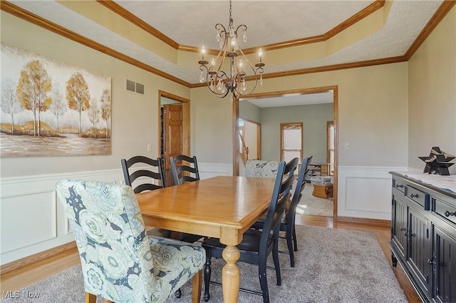 dining room featuring a chandelier, a wainscoted wall, light wood-style flooring, visible vents, and a raised ceiling