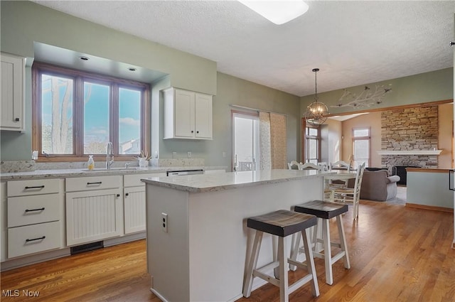 kitchen with white cabinets, light wood finished floors, a sink, a kitchen bar, and open floor plan