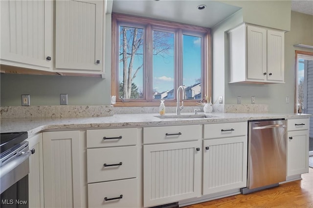 kitchen featuring stainless steel appliances, a sink, white cabinetry, and light stone counters