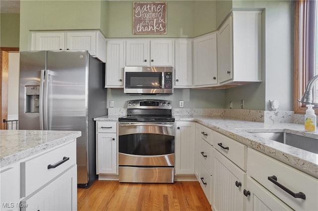 kitchen with white cabinets, stainless steel appliances, a sink, light wood-style floors, and light stone countertops