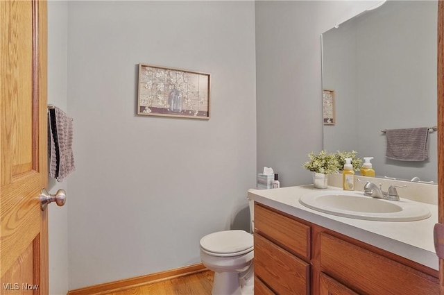 half bath with toilet, vanity, and wood finished floors