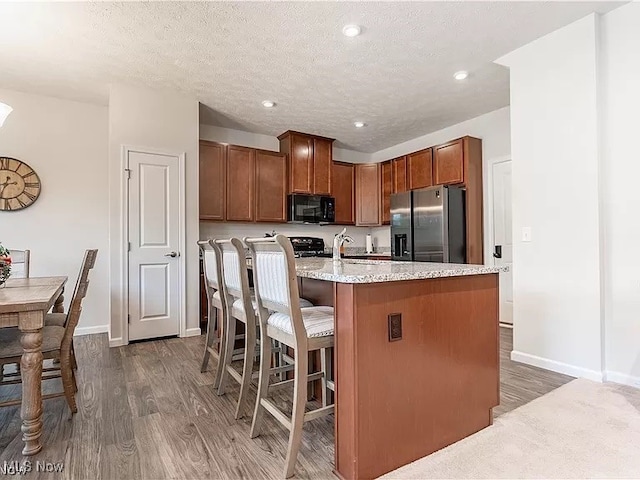 kitchen featuring black microwave, a kitchen island with sink, range, dark wood finished floors, and stainless steel refrigerator with ice dispenser