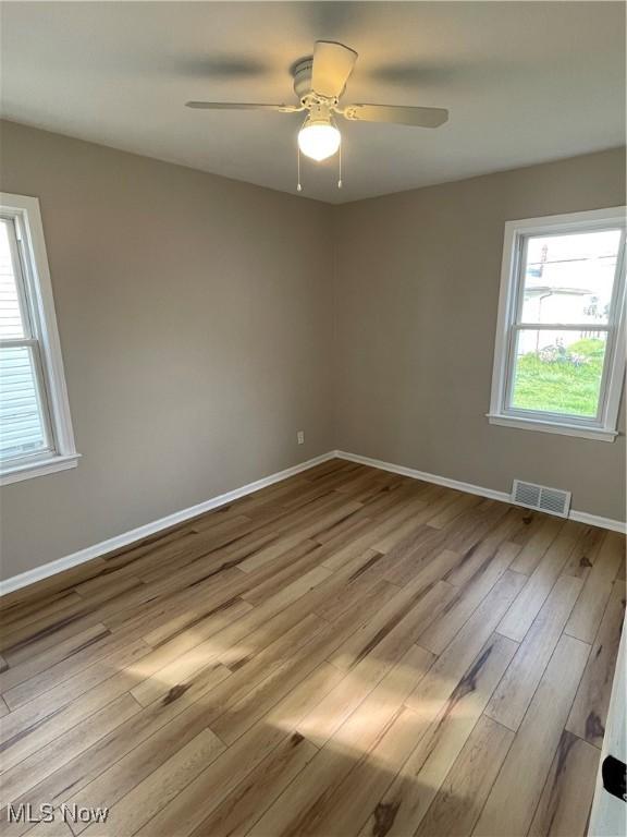 unfurnished room featuring baseboards, a ceiling fan, wood finished floors, and visible vents