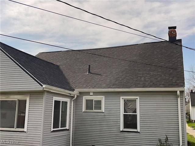 view of home's exterior with roof with shingles and a chimney