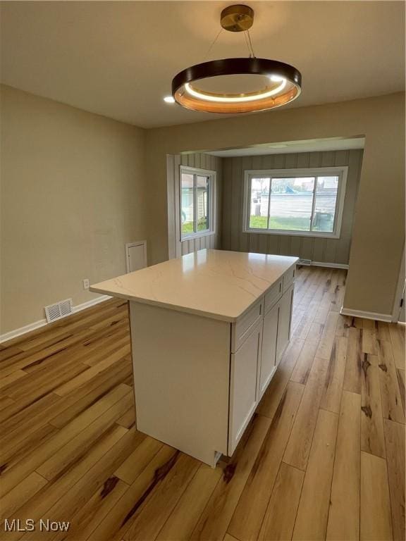 kitchen with white cabinets, light wood finished floors, visible vents, a kitchen island, and baseboards