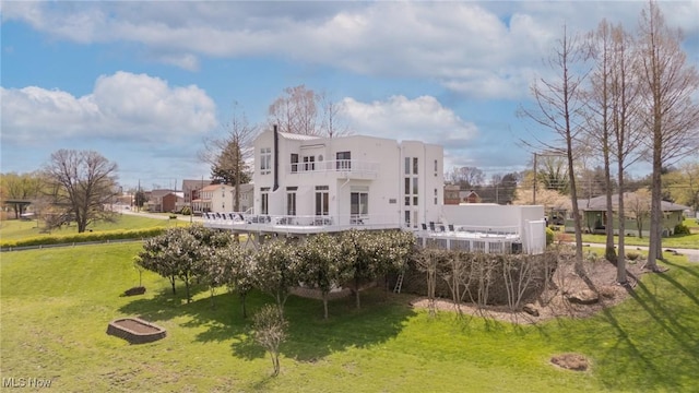 back of house with stucco siding, a lawn, and a balcony