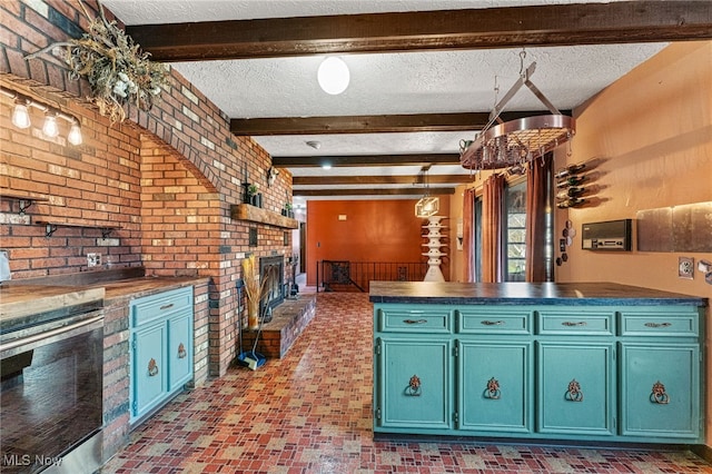 kitchen featuring blue cabinets, beamed ceiling, a fireplace, a textured ceiling, and brick wall