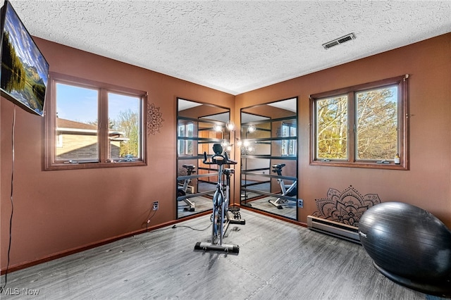 exercise room featuring baseboards, visible vents, a textured ceiling, and plenty of natural light