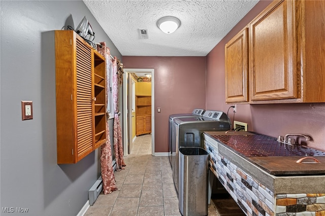 laundry area with a textured ceiling, baseboards, separate washer and dryer, cabinet space, and light tile patterned floors