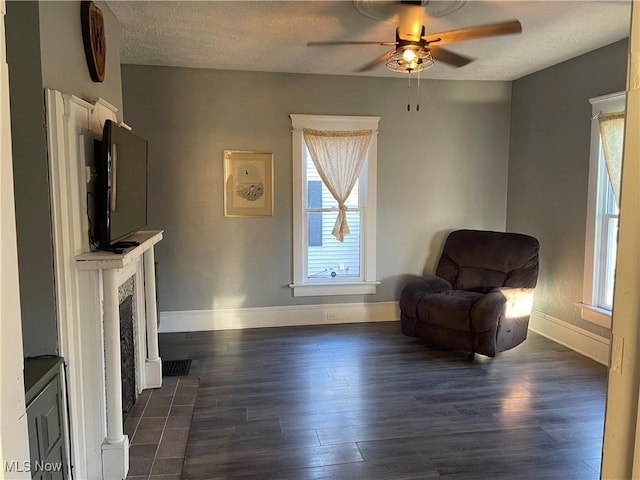 living area featuring dark wood finished floors, ceiling fan, baseboards, and a fireplace with flush hearth