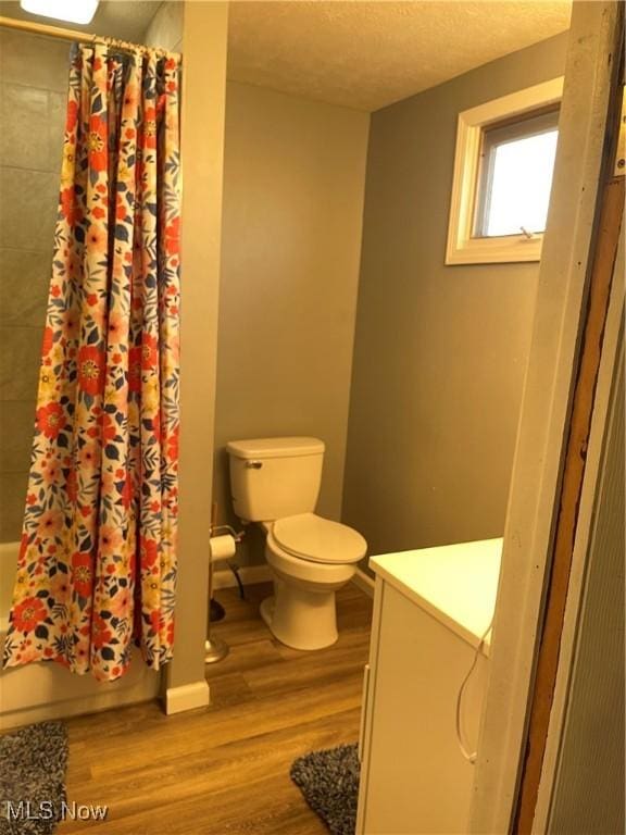 full bathroom with wood finished floors, a textured ceiling, toilet, and shower / bath combination with curtain