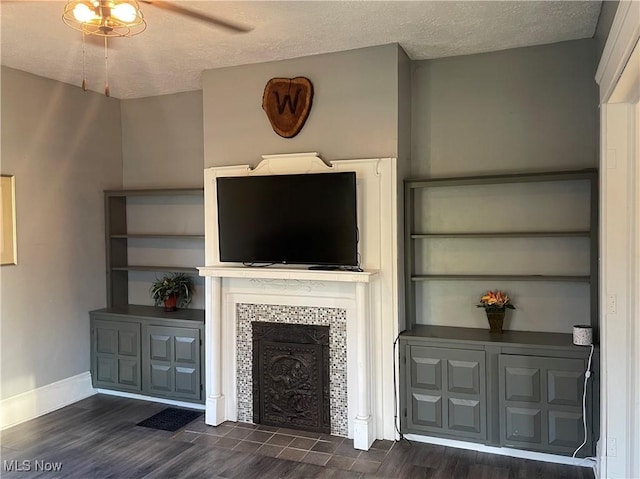unfurnished living room with a tile fireplace, dark wood-style floors, baseboards, a textured ceiling, and ceiling fan